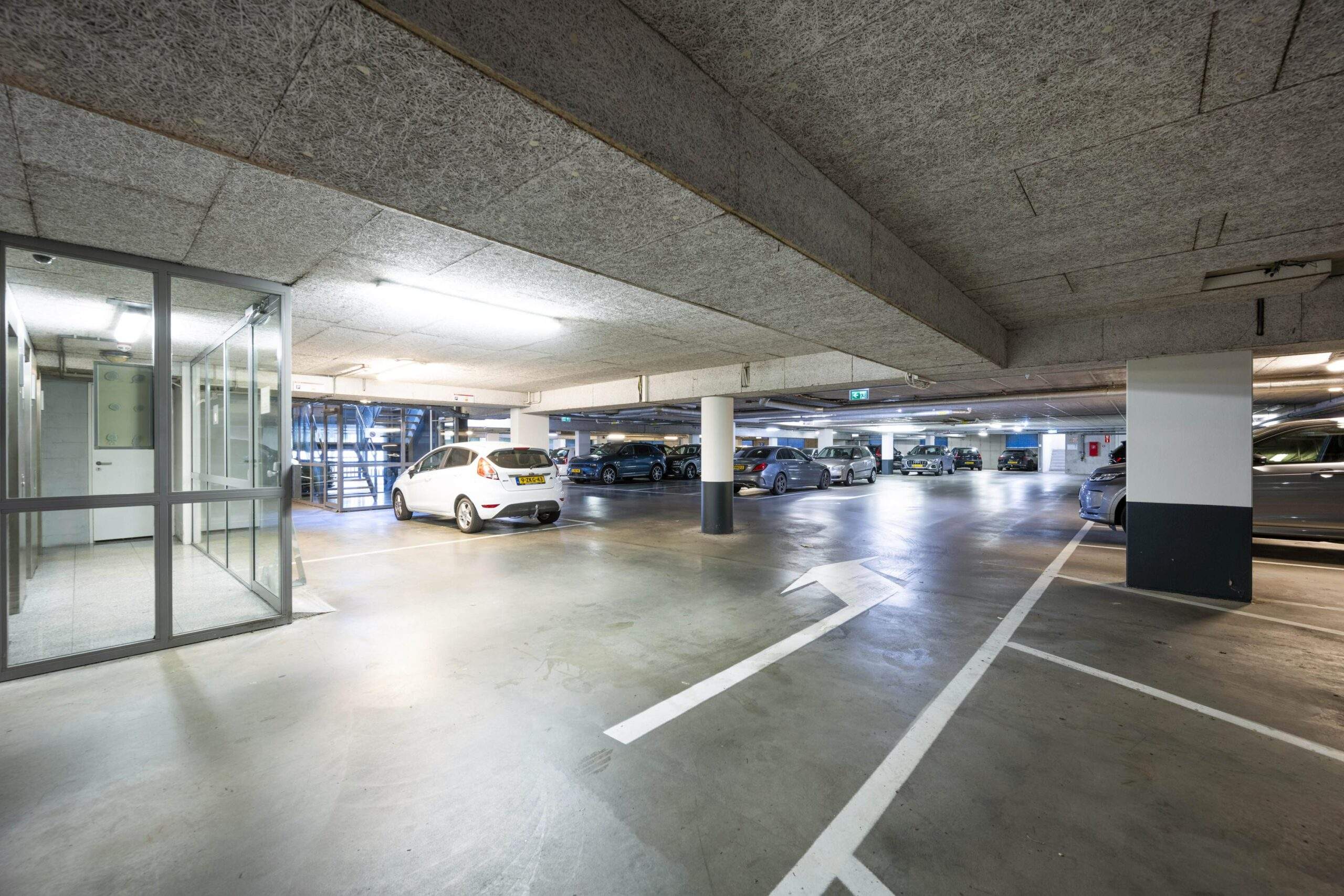 Ondergrondse parkeergarage op het Koningin Wilhelminaplein met geparkeerde auto's en glazen trappenhuis.